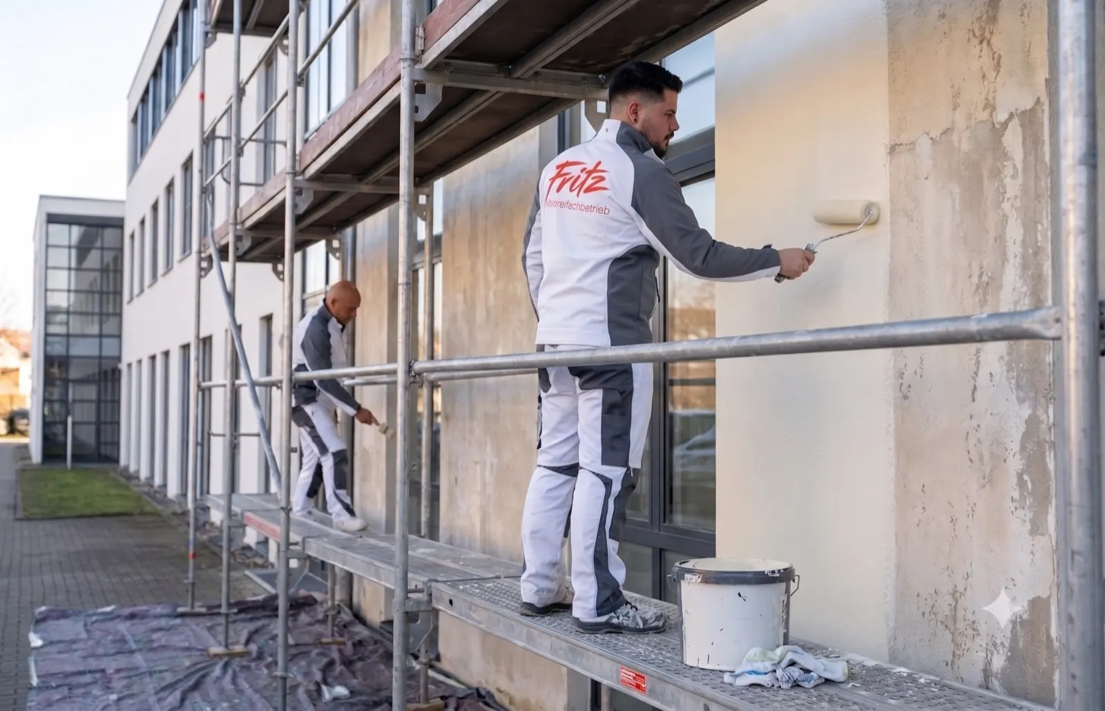 Zwei Maler führen auf einem Gerüst einen Fassadenanstrich an der Aussenwand eines modernen Gebäudes durch