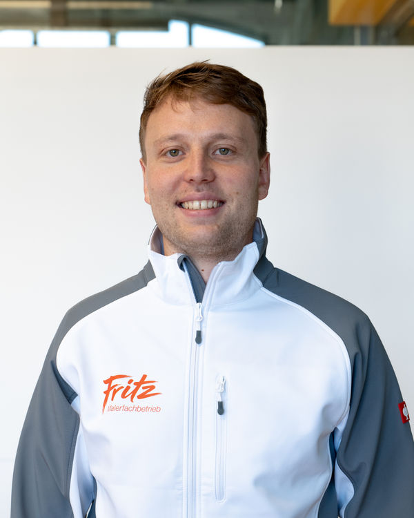 Florian Fritz Vasseur, Geschäftsführer, lächelt in der weissen und grauen Softshell-Jacke des Malerfachbetriebs Fritz