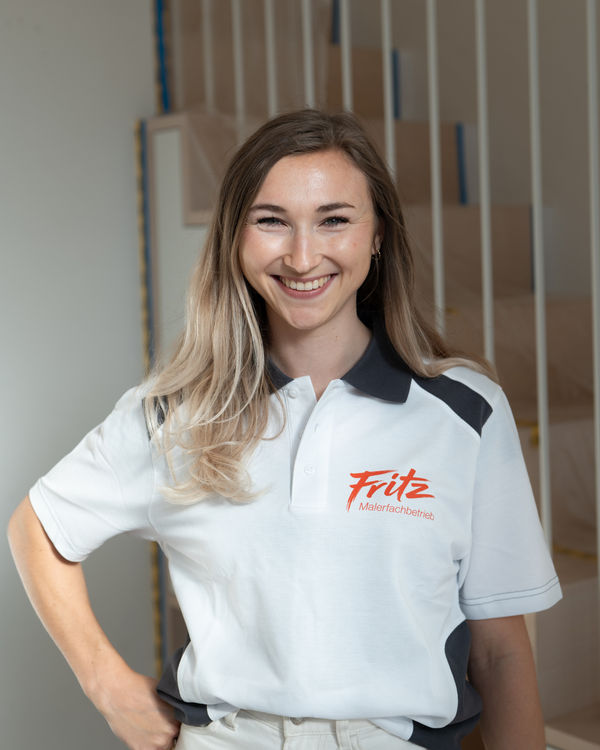 Leona, Planung und Raumdesign, lächelnd im Fritz Malerfachbetrieb Polo-Shirt vor einem unfertigen Holztreppenhaus